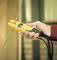A hand is holding a yellow electrical measuring device, displaying a voltage of 120.2 volts and connected with cables.