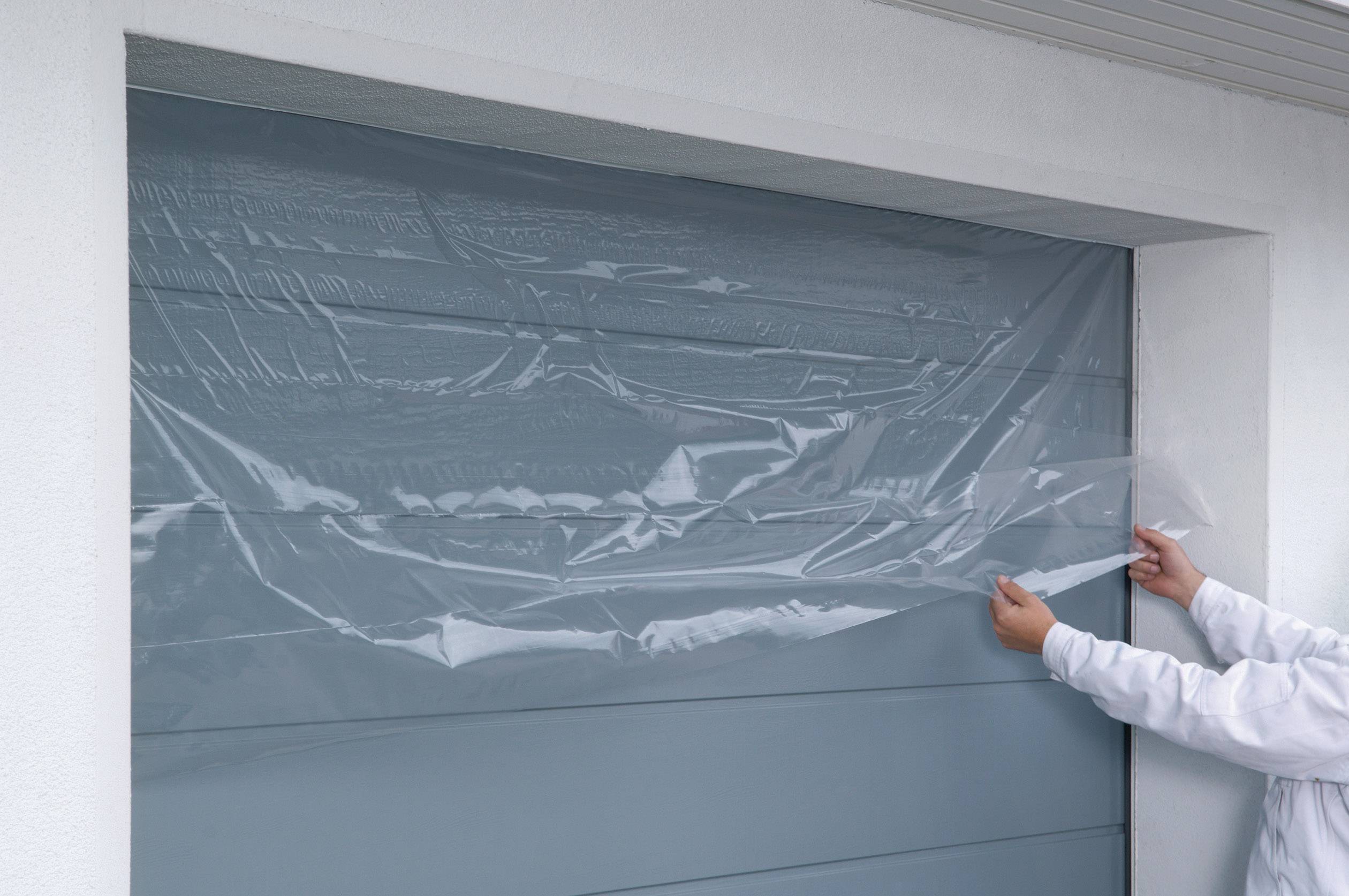 A person is applying a protective film to a garage door.