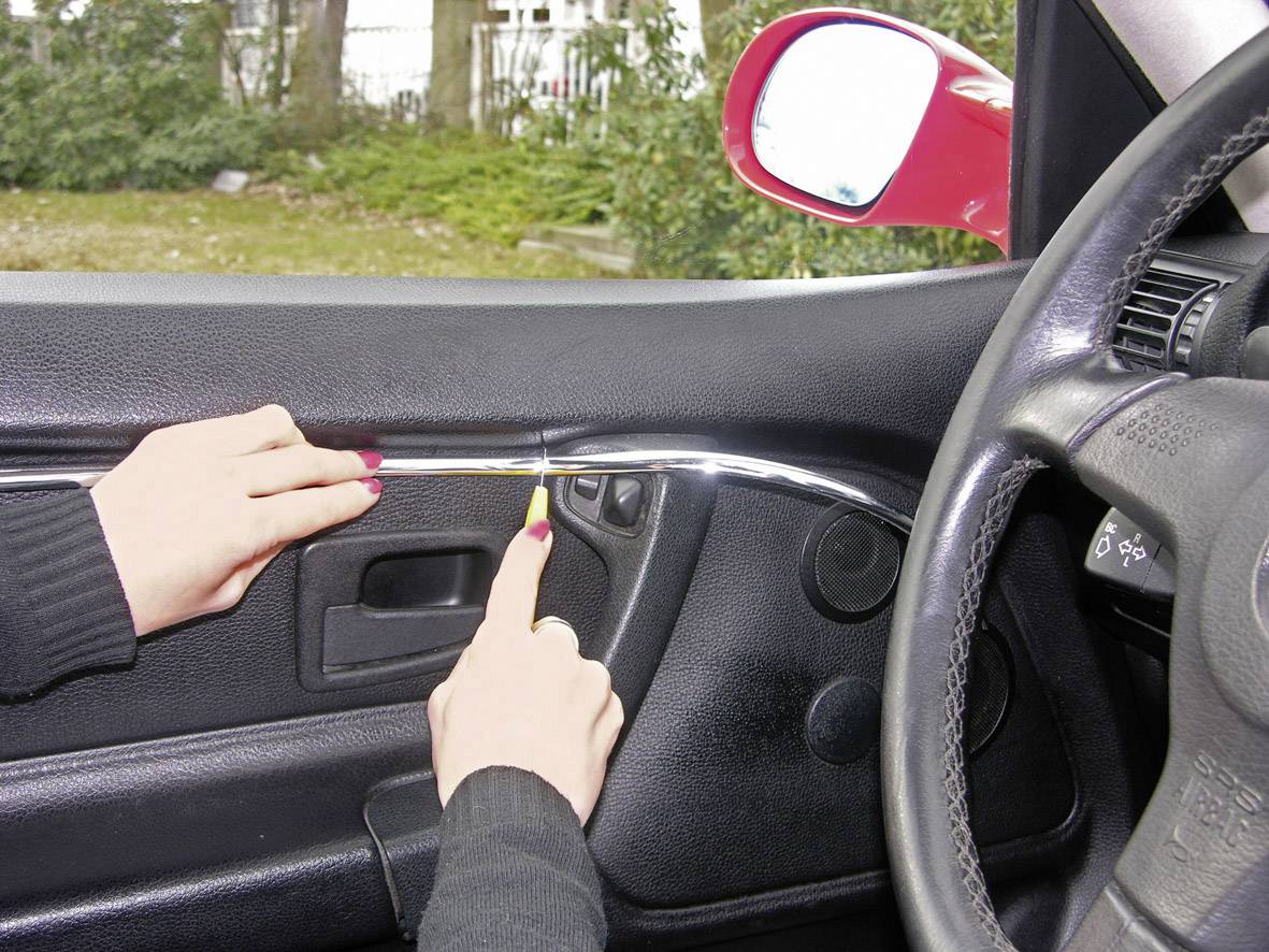 'Hands are using a tool to remove the interior panel of a car door.'
