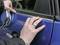 Someone is attaching a decorative trim to the car door of a blue vehicle. Hands are pressing the trim firmly and aligning it.
