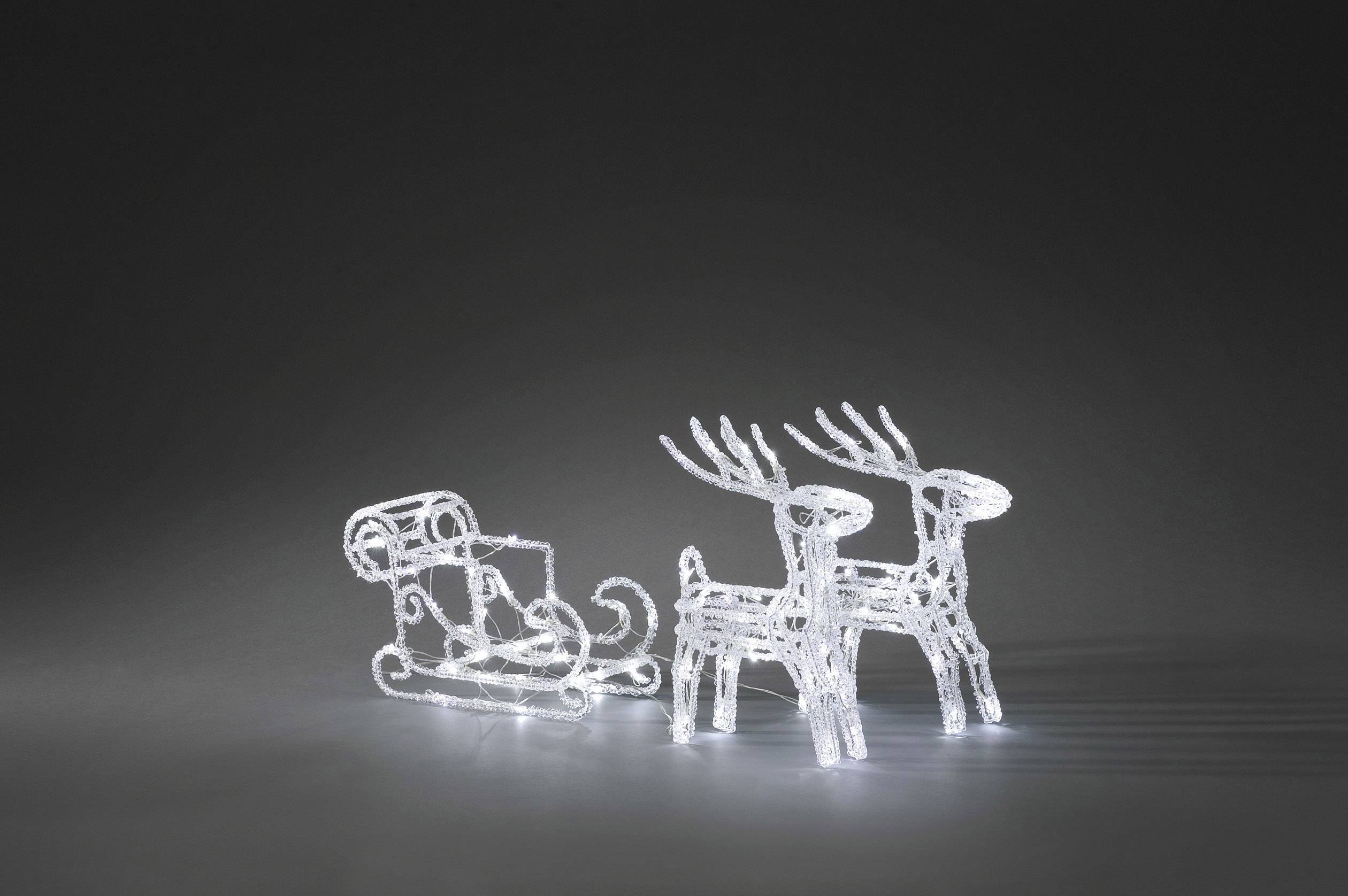 Two illuminated reindeer figures pulling a sleigh, positioned against a dark background. Christmas decoration.