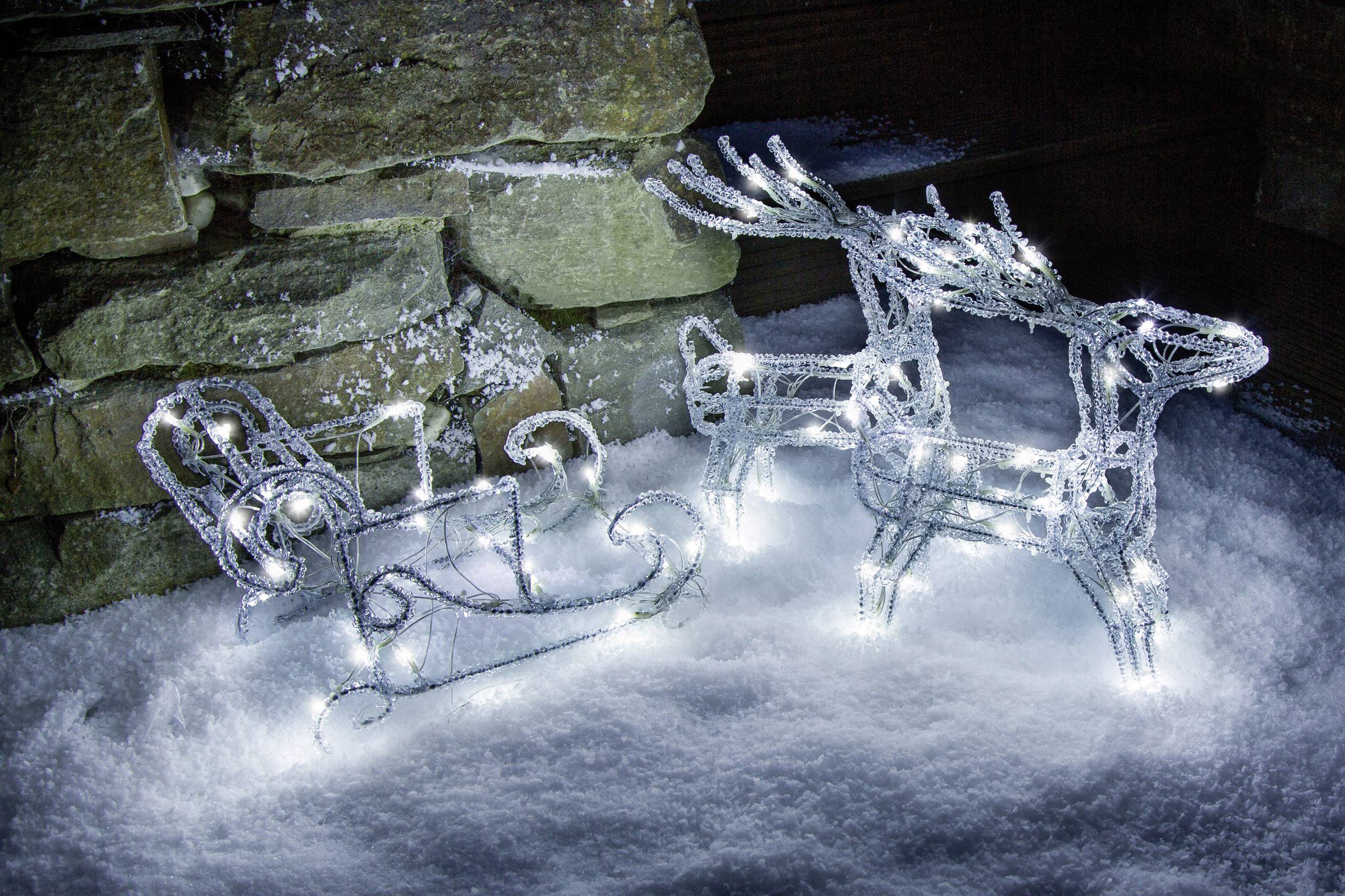 String of lights in the shape of a reindeer and sleigh in the snow. Stones are visible in the background. Festive winter decoration.