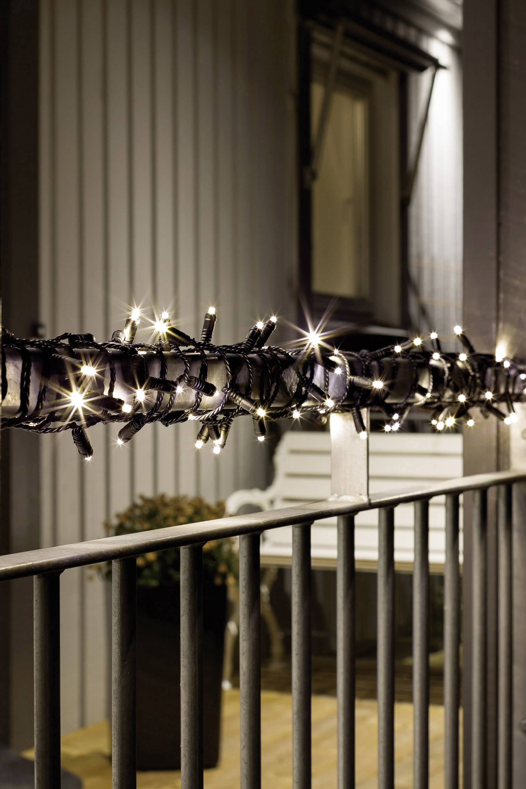 A string of fairy lights is wound around the balcony railing. It gently illuminates the surroundings, with a window and a bench visible in the background.
