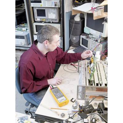 A person in a technical laboratory is working on a circuit board with electronic measuring devices and tools on the table.