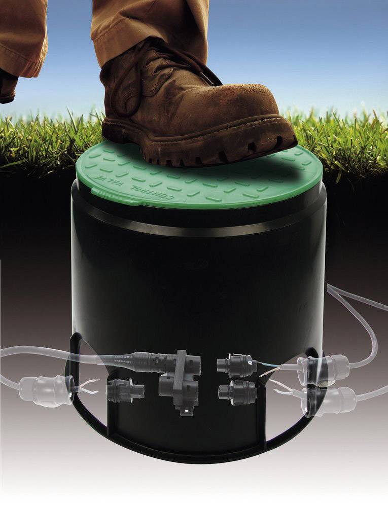 A person in sturdy shoes steps onto a round, green lid of a black cylinder to which pipes are connected.