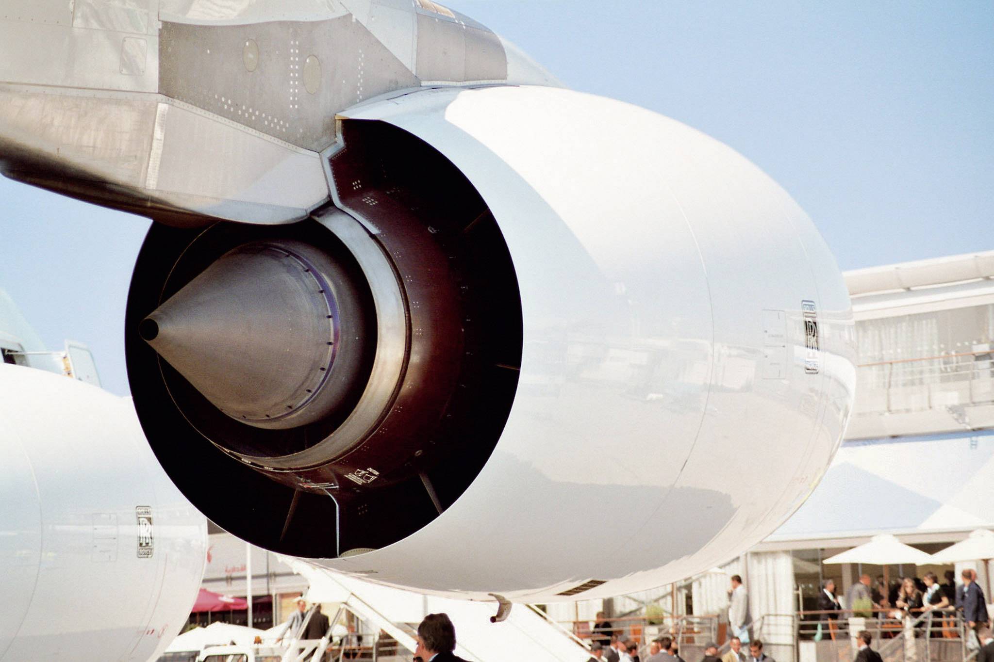 Close-up of an aircraft engine displayed on an exhibition site. Visitors and buildings can be seen in the background.