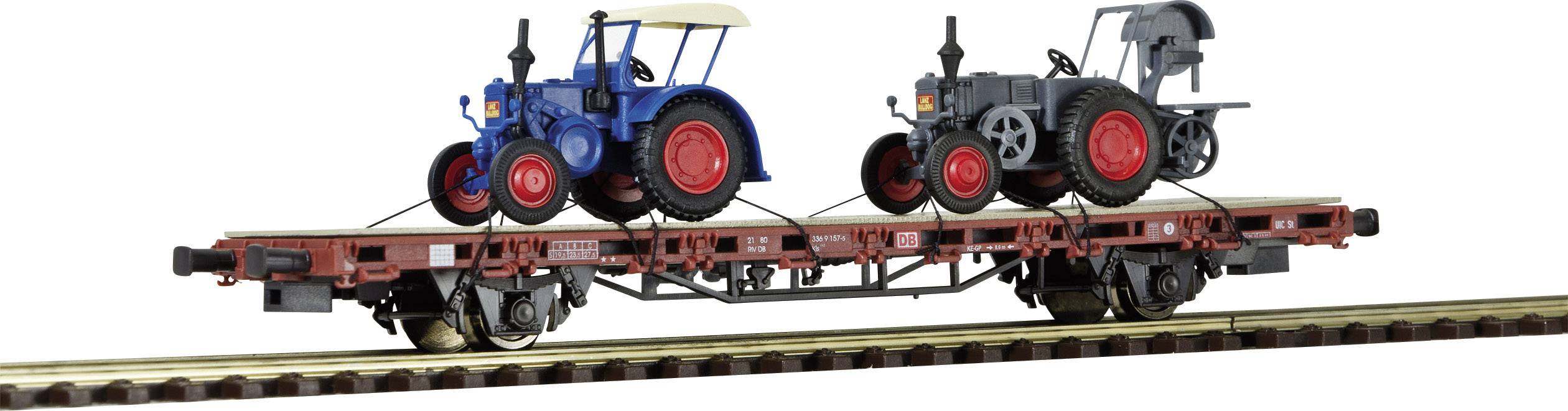 Two small tractor models, one blue and one grey, are standing on a model goods wagon on a model railway track.
