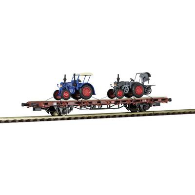 Two small tractor models, one blue and one grey, are standing on a model goods wagon on a model railway track.