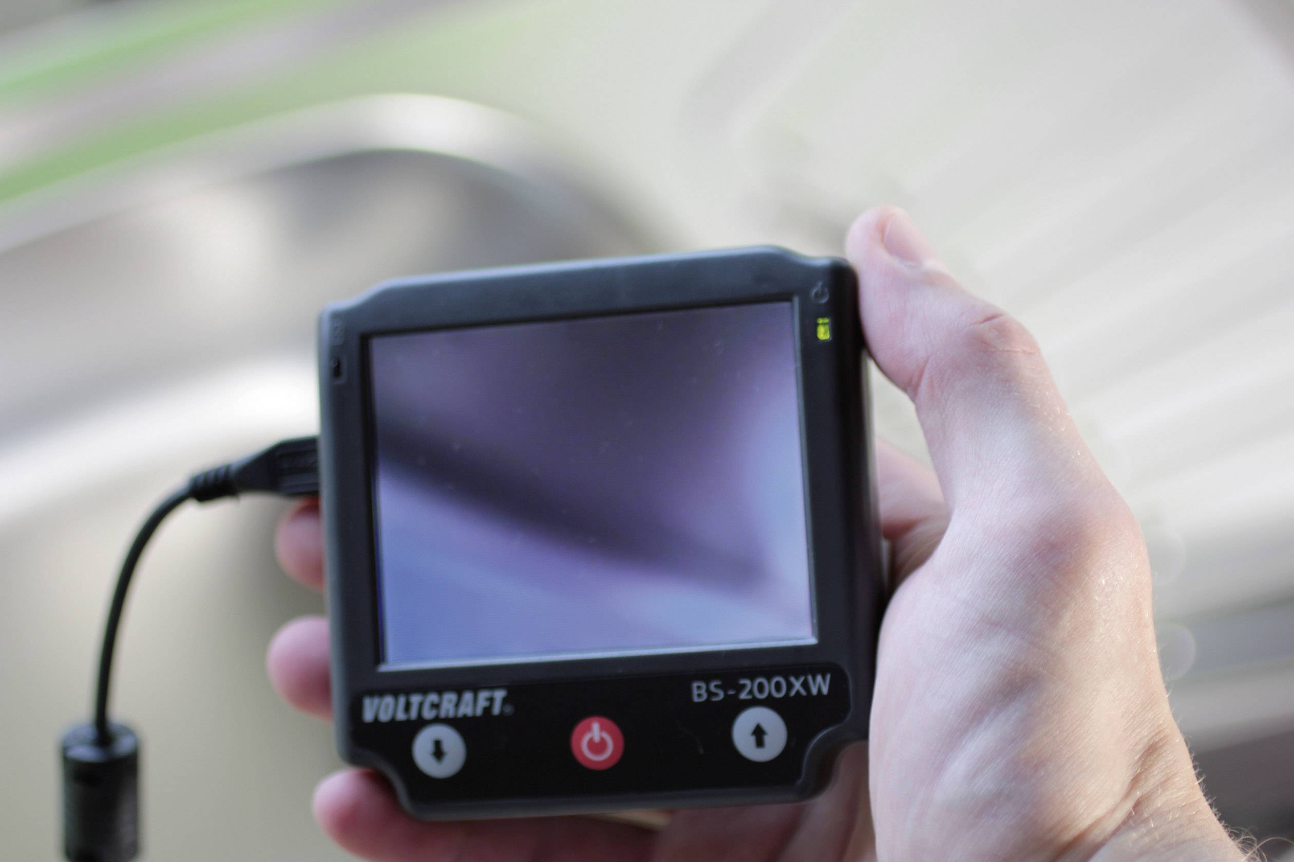 A person is holding a Voltcraft BS-200XW endoscope with a blank display. The device appears to be switched off or inactive.