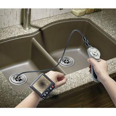 A person is using an inspection camera with a monitor to check the drain underneath the sink. The device is showing the interior of the pipe.