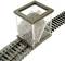 A container of grey ballast is positioned on a model railway track to distribute the stones evenly between the sleepers.