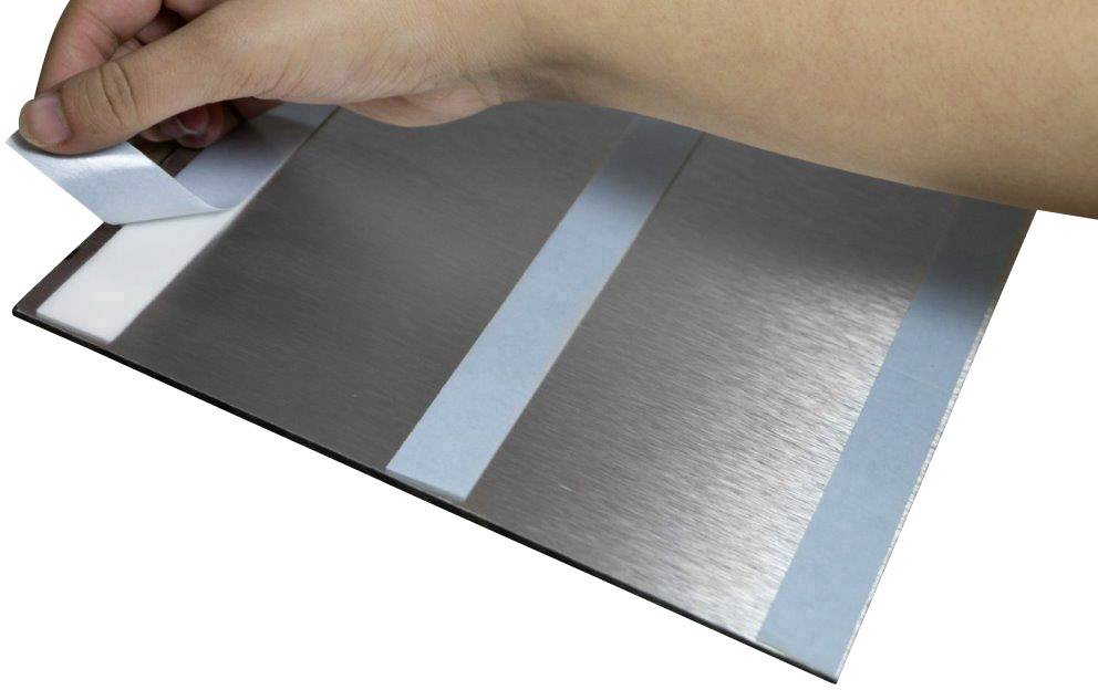 A hand is removing the protective film from a metal sheet with adhesive strips.
