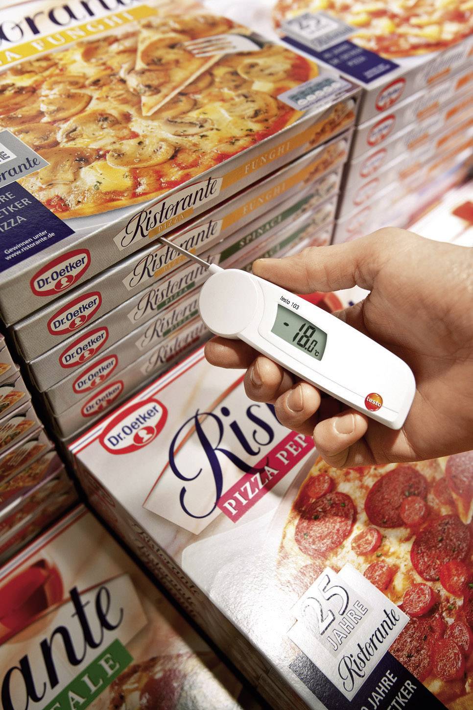 A hand measures the temperature of a frozen pizza packet in the supermarket freezer cabinet using a digital thermometer.
