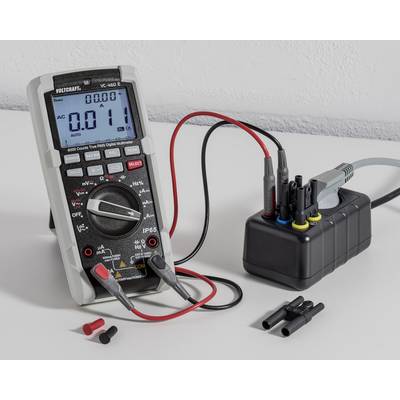 Digital multimeter and connection cables on a table, showing a voltage of 0.11 V. Connected to a device with coloured sockets.
