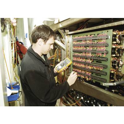 A technician is checking electrical connections with a multimeter on a control panel in a technical room.