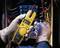 A person wearing safety gloves is measuring the voltage in an electrical control box with a yellow multimeter.