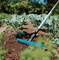 A blue garden fork is tilling the soil of a vegetable garden with young plants beneath a blue sky.