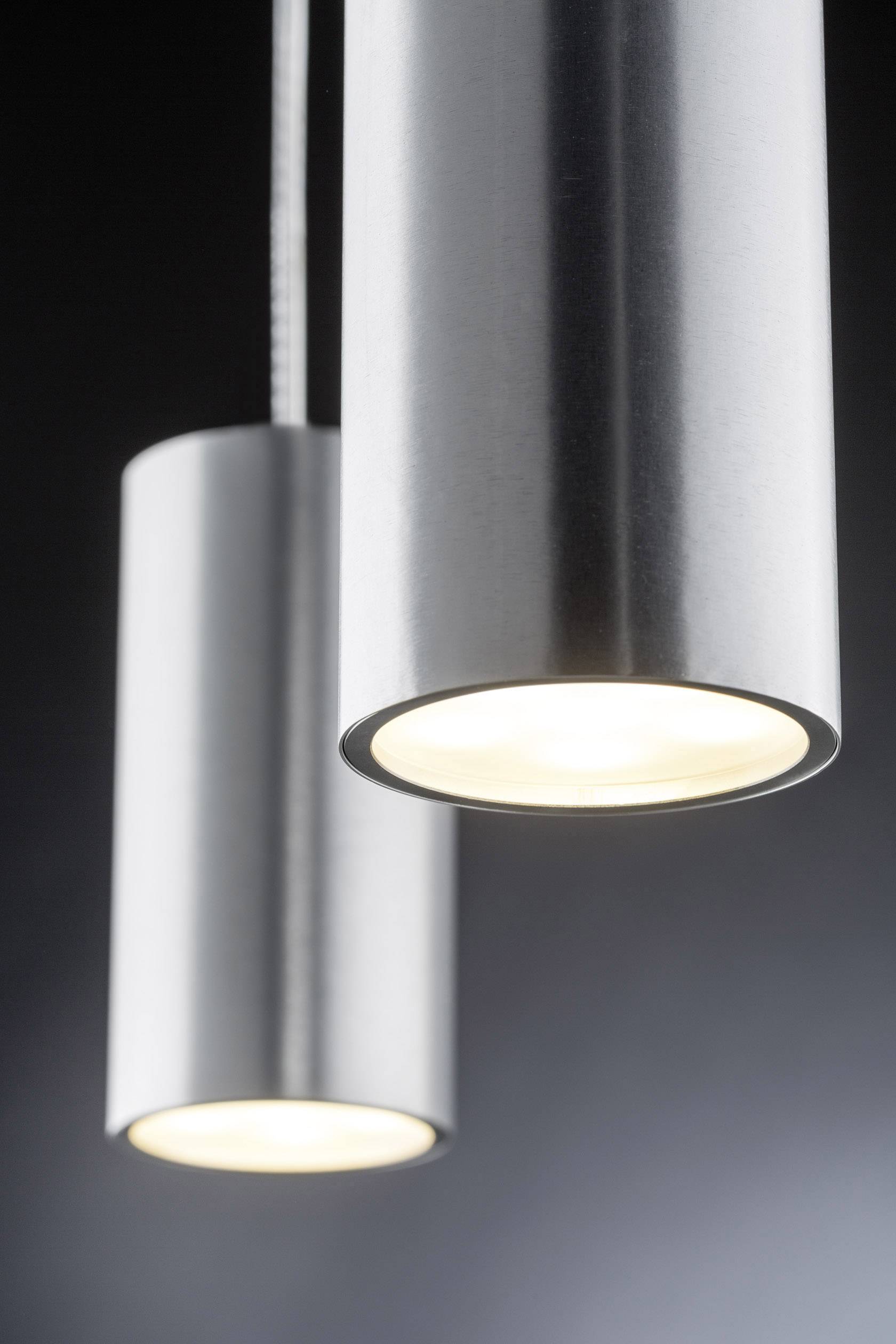 Two modern, cylindrical ceiling lights made of metal hang from cables against a dark background. They emit warm light.