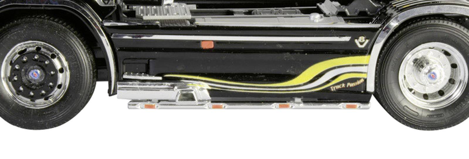 A black lorry viewed from the side, featuring yellow and white stripes and silver details, partially showing tyres and decorative elements.