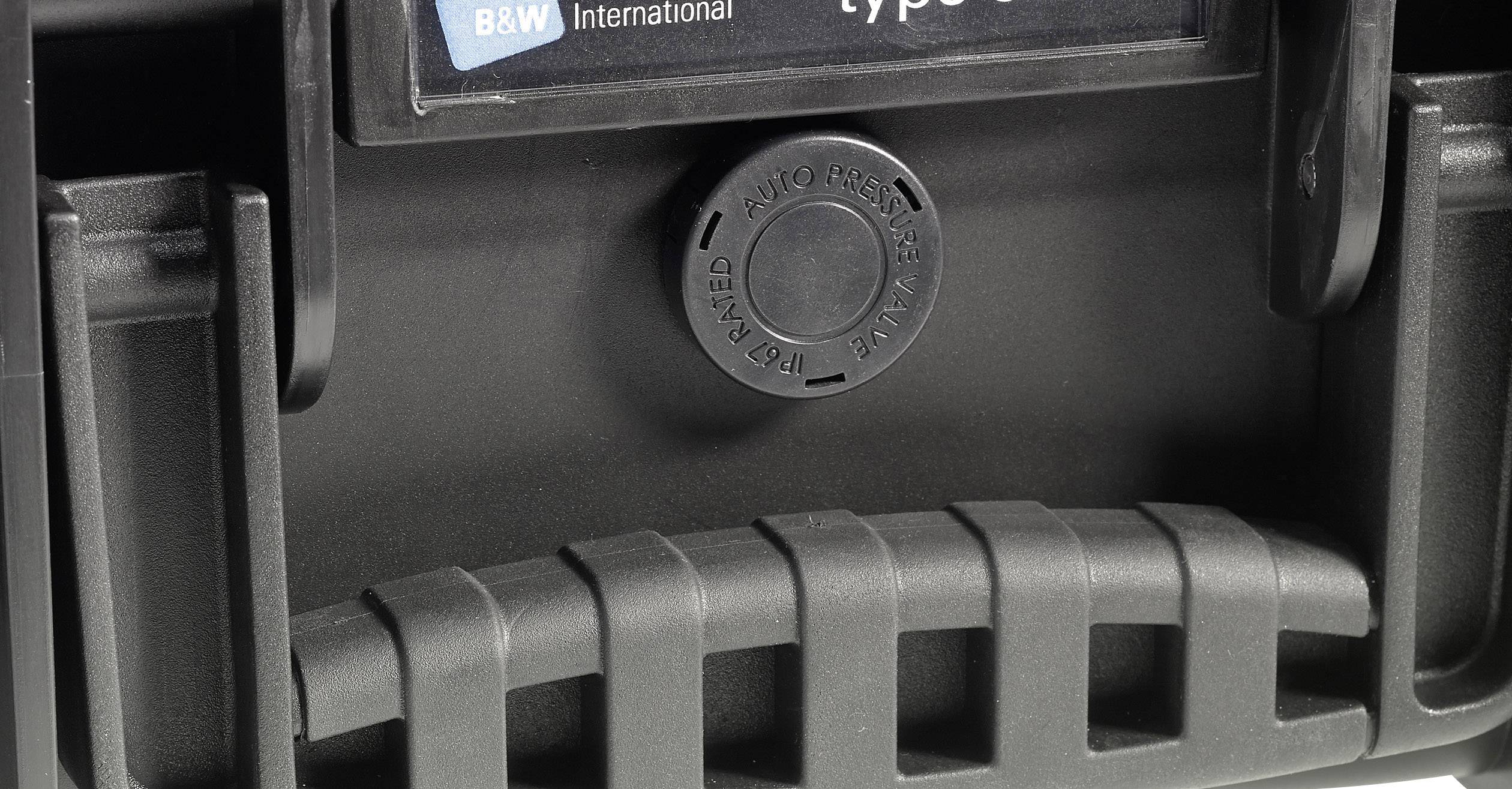 Handle of a black, robust suitcase with a round pressure equalisation opening in the centre, with the B&W International logo underneath.