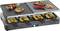 Raclette grill with meat, vegetables and prawns on the griddle plate. Underneath, melted cheese in small pans.