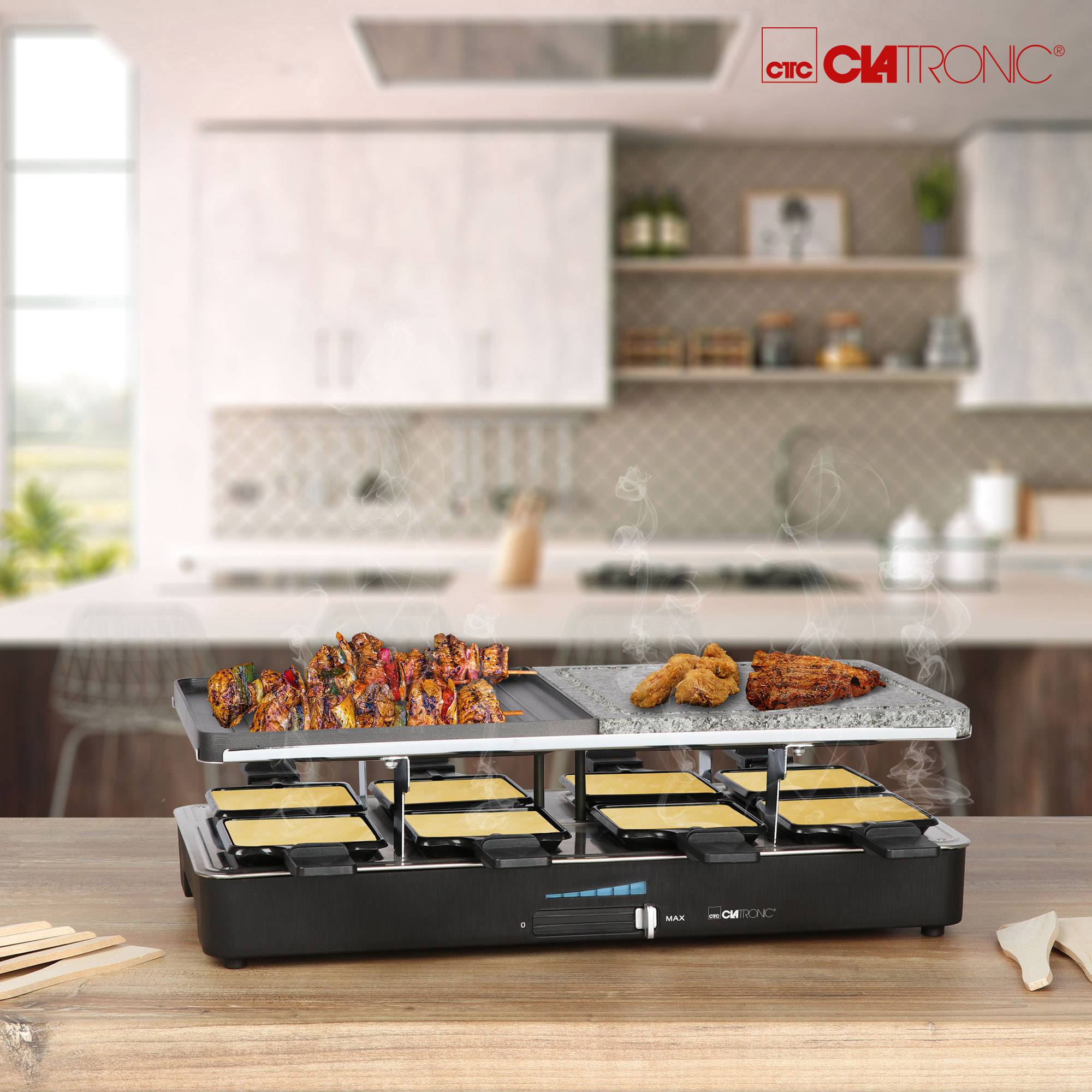 A raclette grill with hot plates laden with meat, vegetables, and melted cheese sits on a kitchen table. Kitchen cupboards are visible in the background.