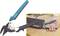 A tin snips with a blue-black handle cuts a metal sheet. The tool is lying on a wooden table.
