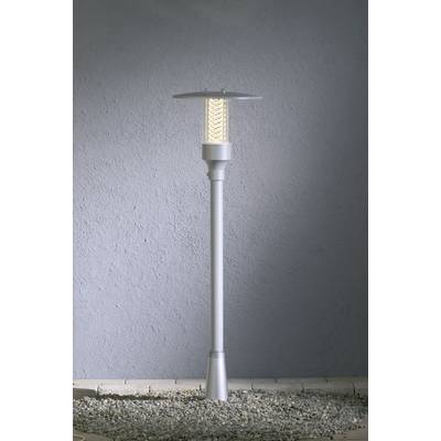 Silver, modern floor lamp illuminates on grey flooring in front of a grey wall. Minimalist design emphasises understated elegance.