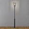 Floor lamp with classic design, illuminating a dark environment, standing on a wooden floor in front of a grey wall.