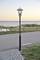 A lantern stands beside a gravel path by the sea. In the background is a calm, vibrant sunset with a cloudless sky.