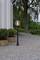 A sphere lamp on a gravel path beside a white building. Next to it are plants in wooden barrels, with trees visible in the background.