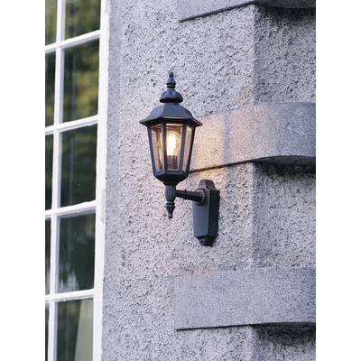 Exterior wall lantern made of black metal with an illuminated light bulb mounted on a textured stone wall beside a window.