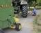A man is inflating the tyre of a green agricultural machine. The machine is standing on a paved path.