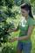 Woman in a green T-shirt cutting leaves from a tree in a sunny garden.