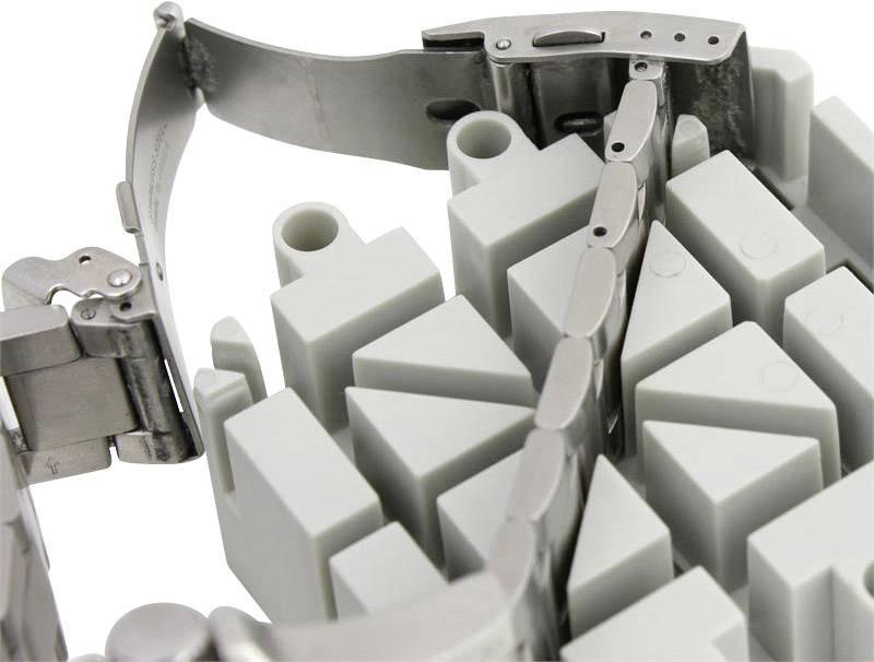 A greatly enlarged image of a metal watch strap clasp, lying on a white, serrated surface, revealing the details of its mechanism.