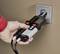 A hand is holding a voltage tester against a socket to check the electrical supply.