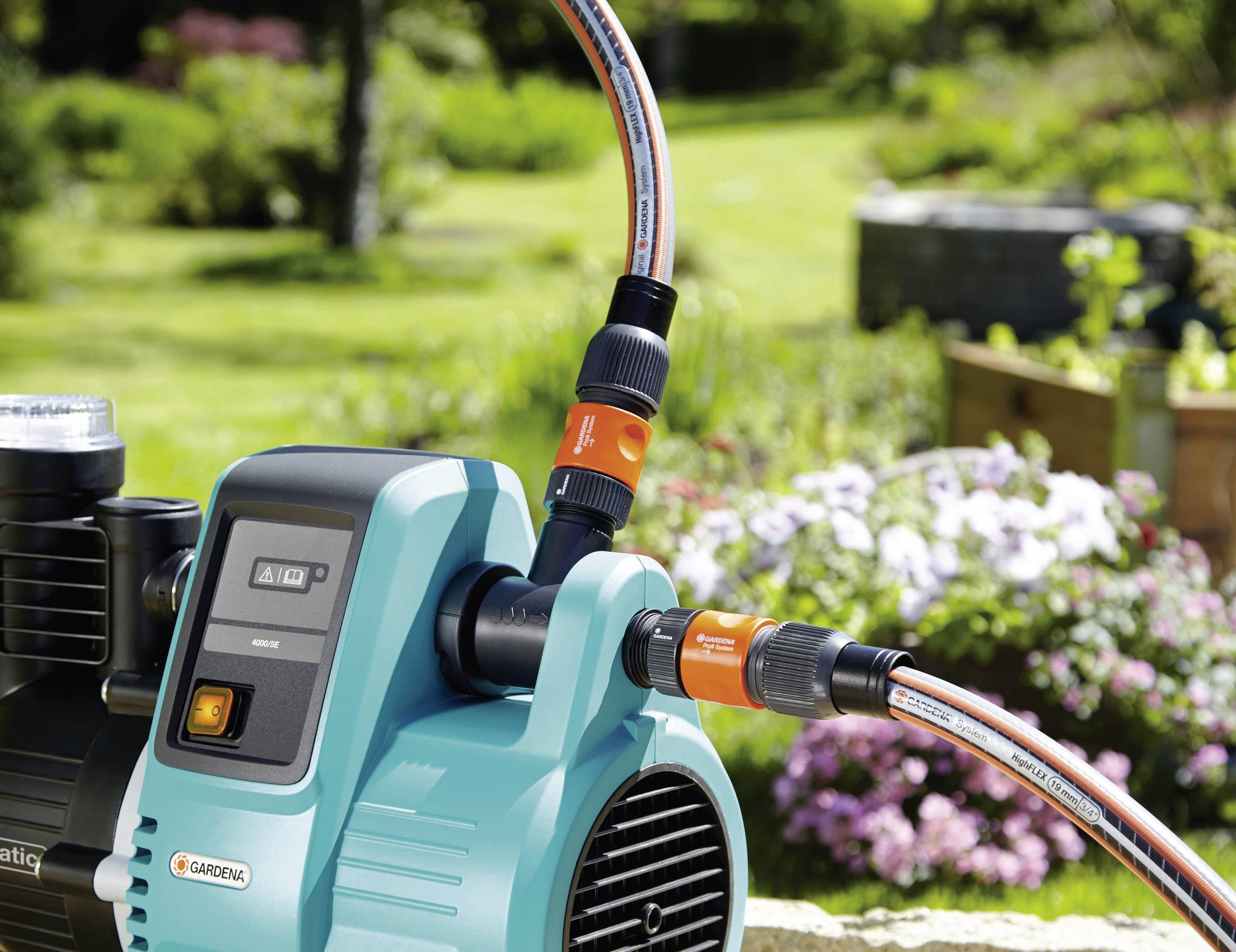 A blue water pump with connected hoses in the garden. Flowers and plants in the background.