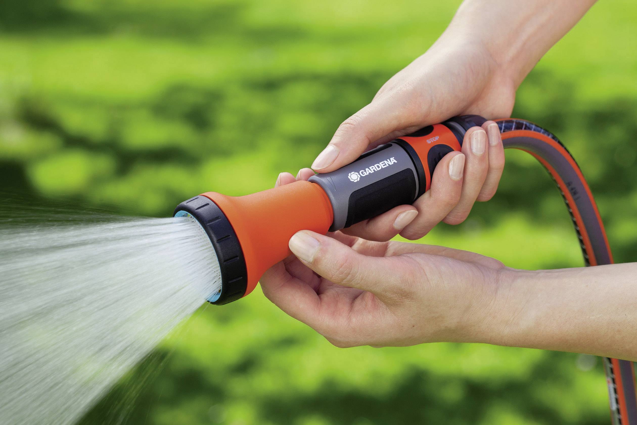 Someone is holding a garden hose with a spray nozzle and watering a lawn. The hose is orange with black details.