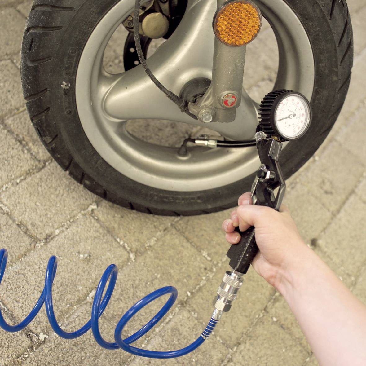 The tyre of a vehicle is being checked with a tyre pressure gauge. A hand is holding the pressure gauge against the valve.