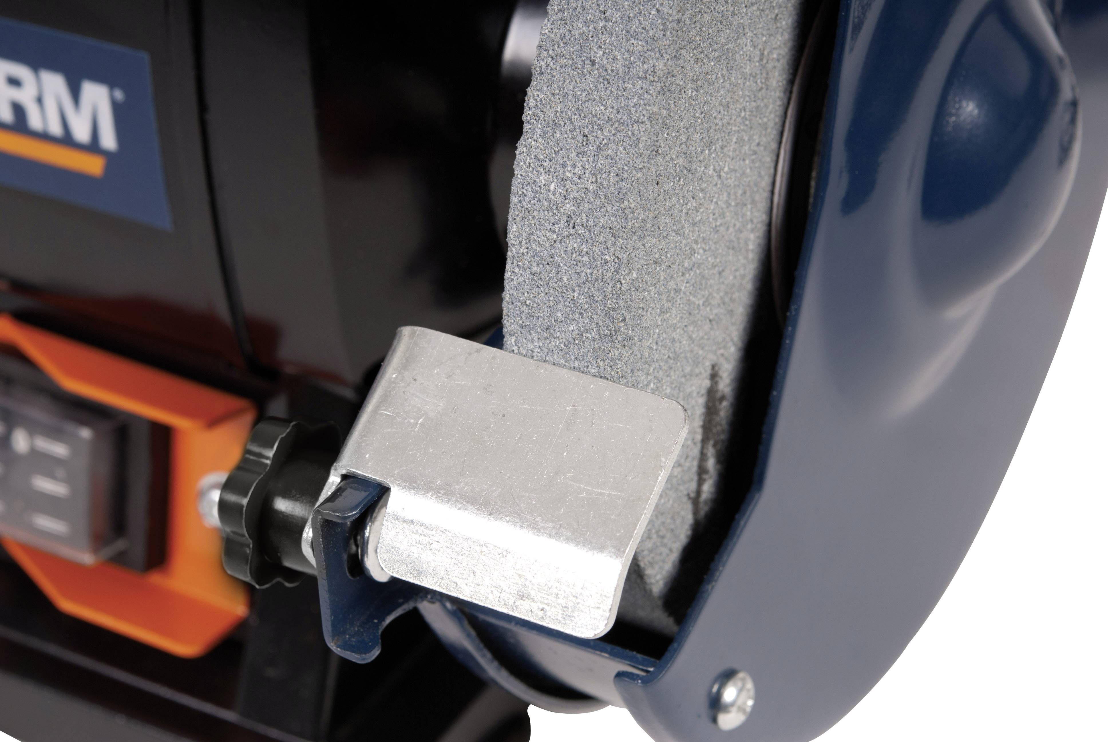 Close-up of a grinding machine with a circular grinding wheel and mounting. A switch and parts of the machine casing are visible.
