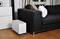 A white air humidifier is standing on a wooden floor next to a black sofa with white and brown cushions in a living room.
