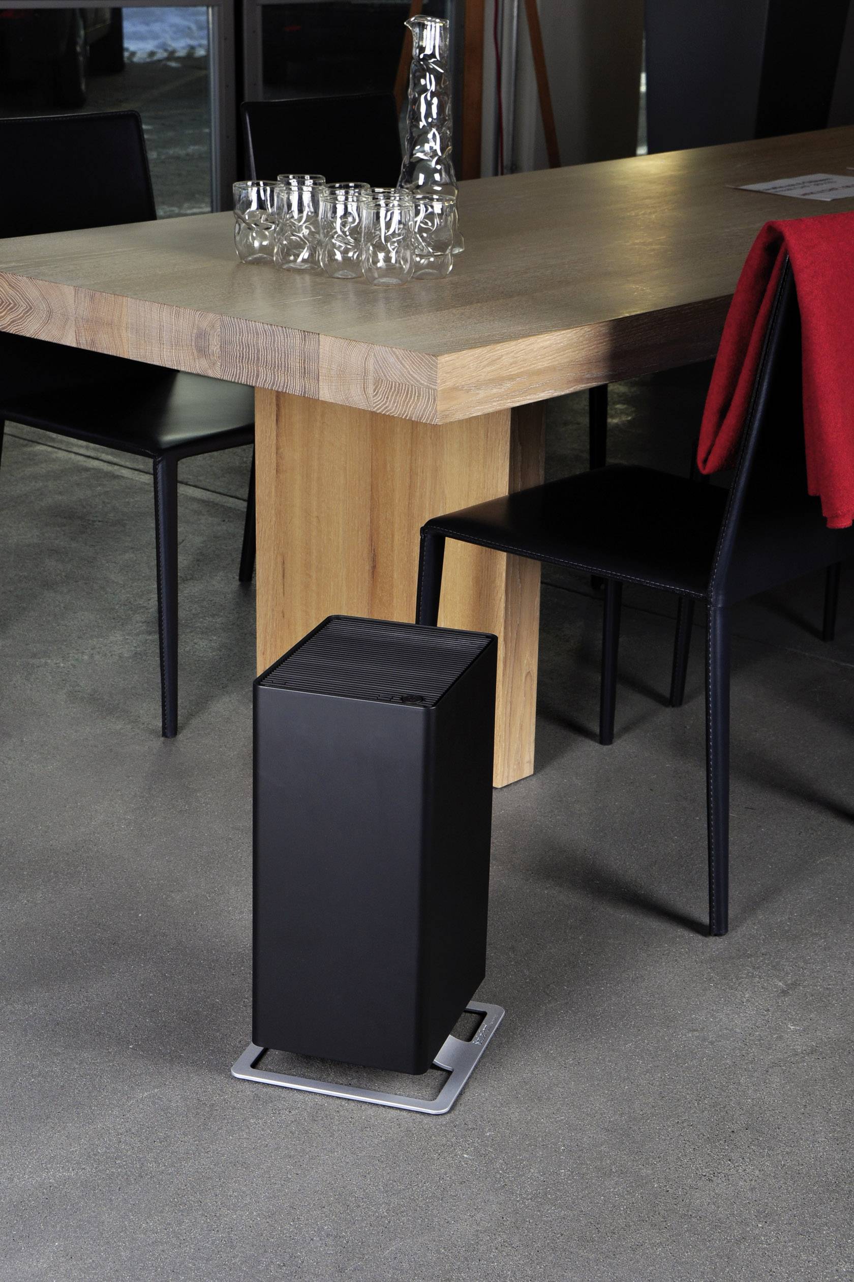 A modern radiator stands next to a wooden table with glasses on it. A red cloth hangs over the chair.