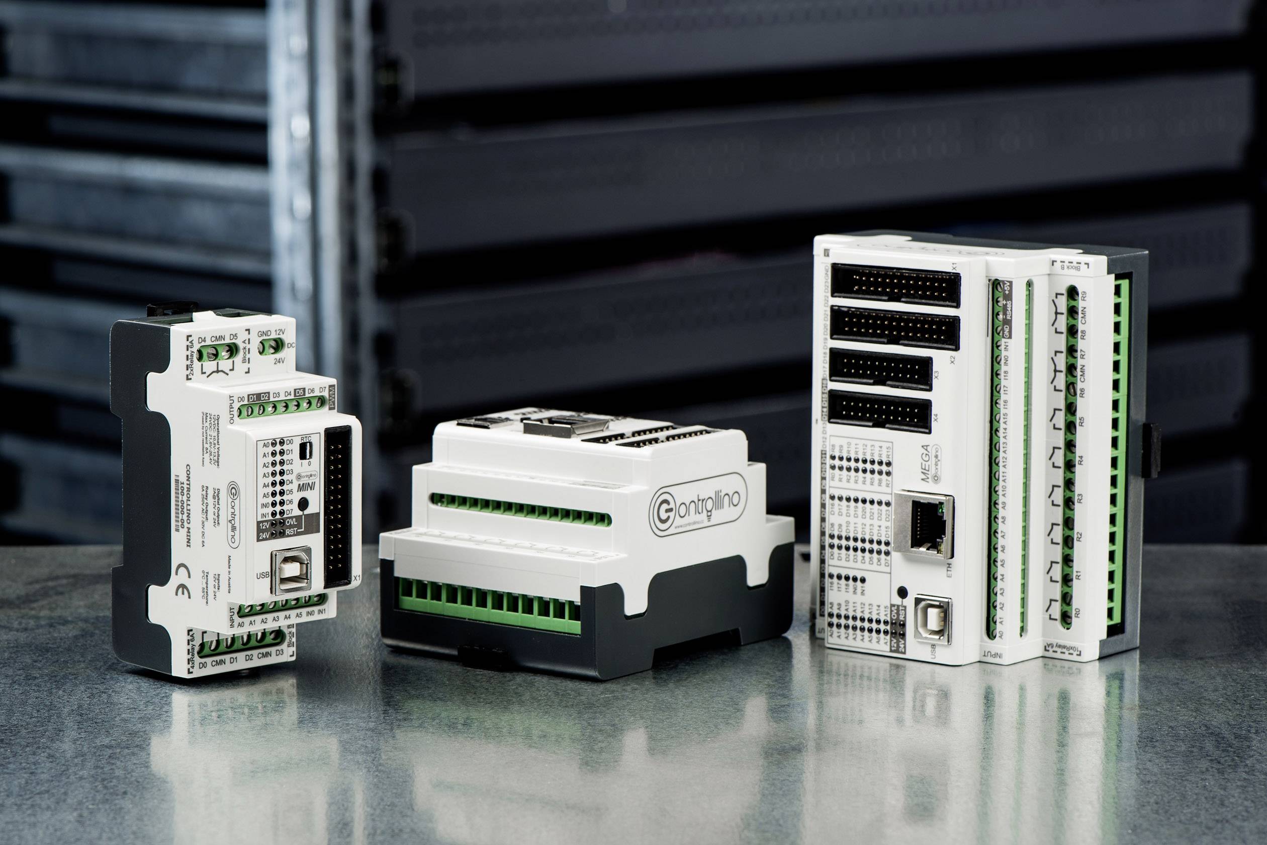 Three different industrial control units on a metallic table, with additional devices visible in the background.