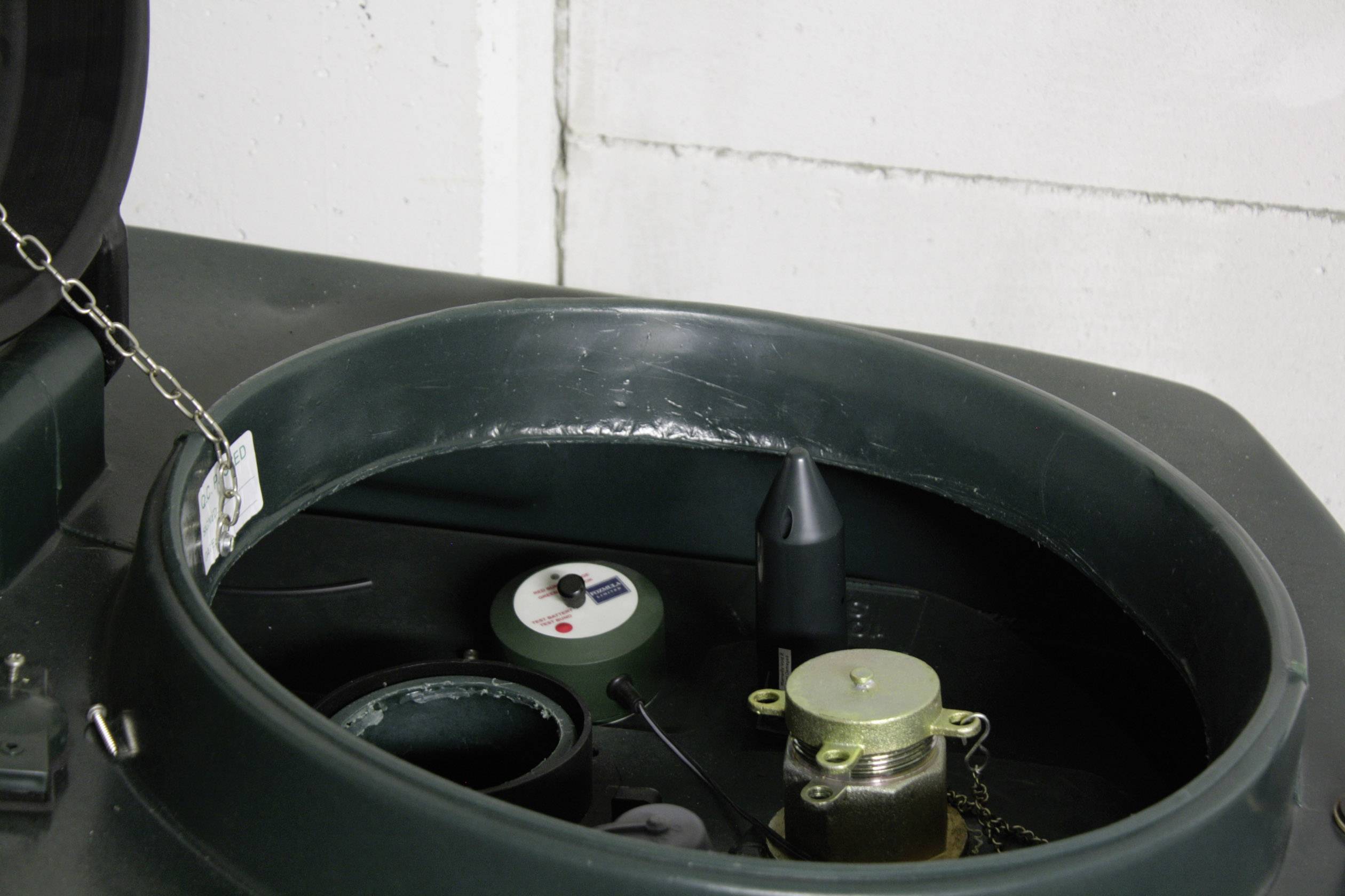 Opening of a green tank with measuring devices and sensors inside. Chain lock on the left. Rectangular recess on the right in the background.