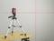A laser levelling device mounted on a tripod projects red lines onto a wall, indicating horizontal and vertical alignments.