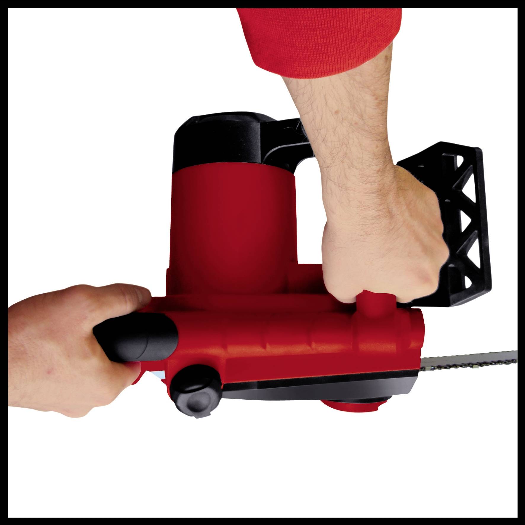 A person is holding an electric chainsaw with a red casing, gripping it with both hands and ready for use.