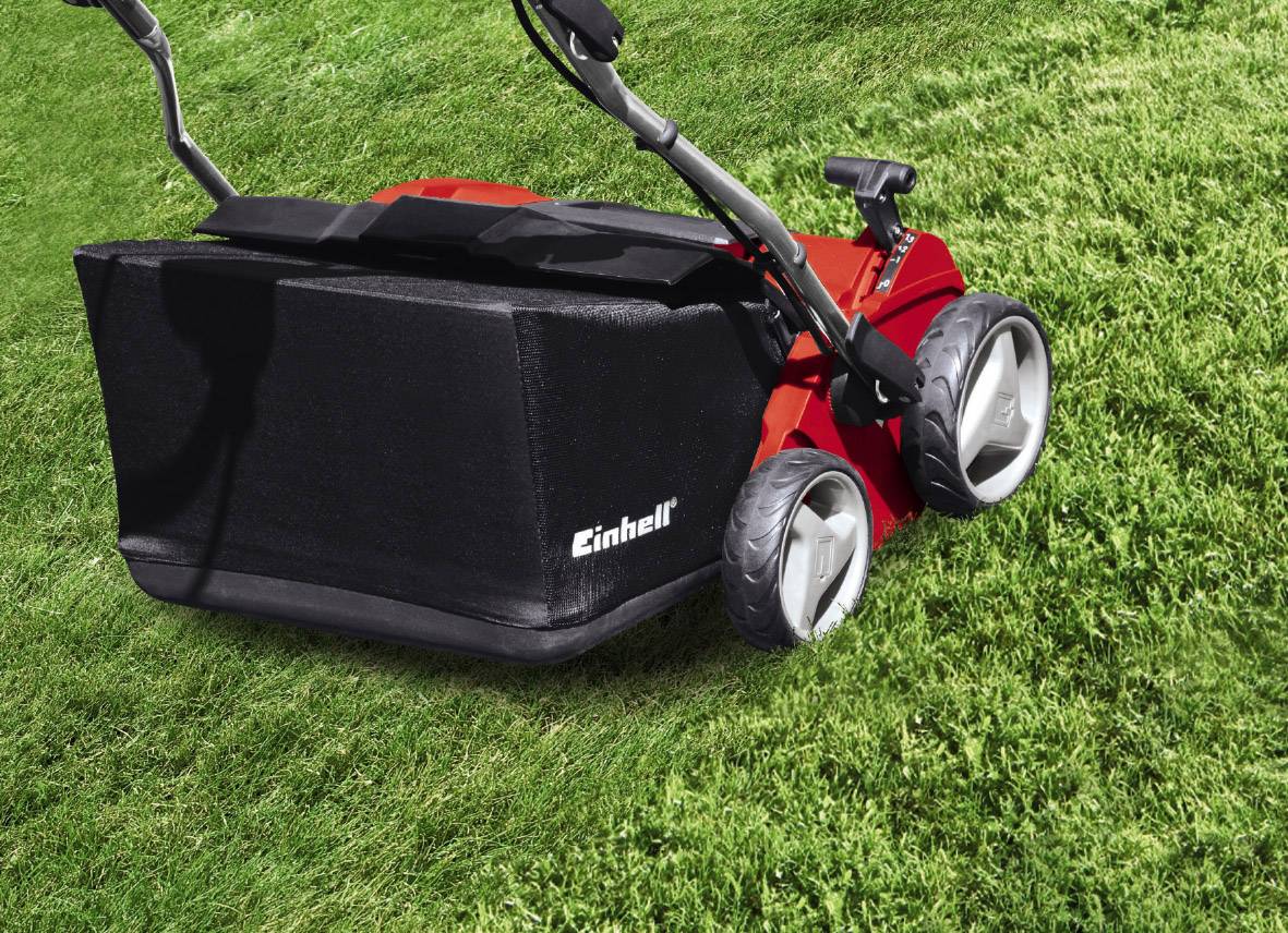 A red lawnmower with large, grey wheels stands on a green lawn. A grass collector is attached in the background.