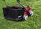 A red lawnmower with large, grey wheels stands on a green lawn. A grass collector is attached in the background.