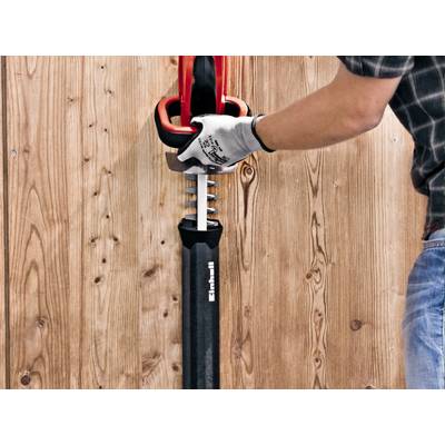 A person is operating a red reciprocating saw mounted on a wooden surface.