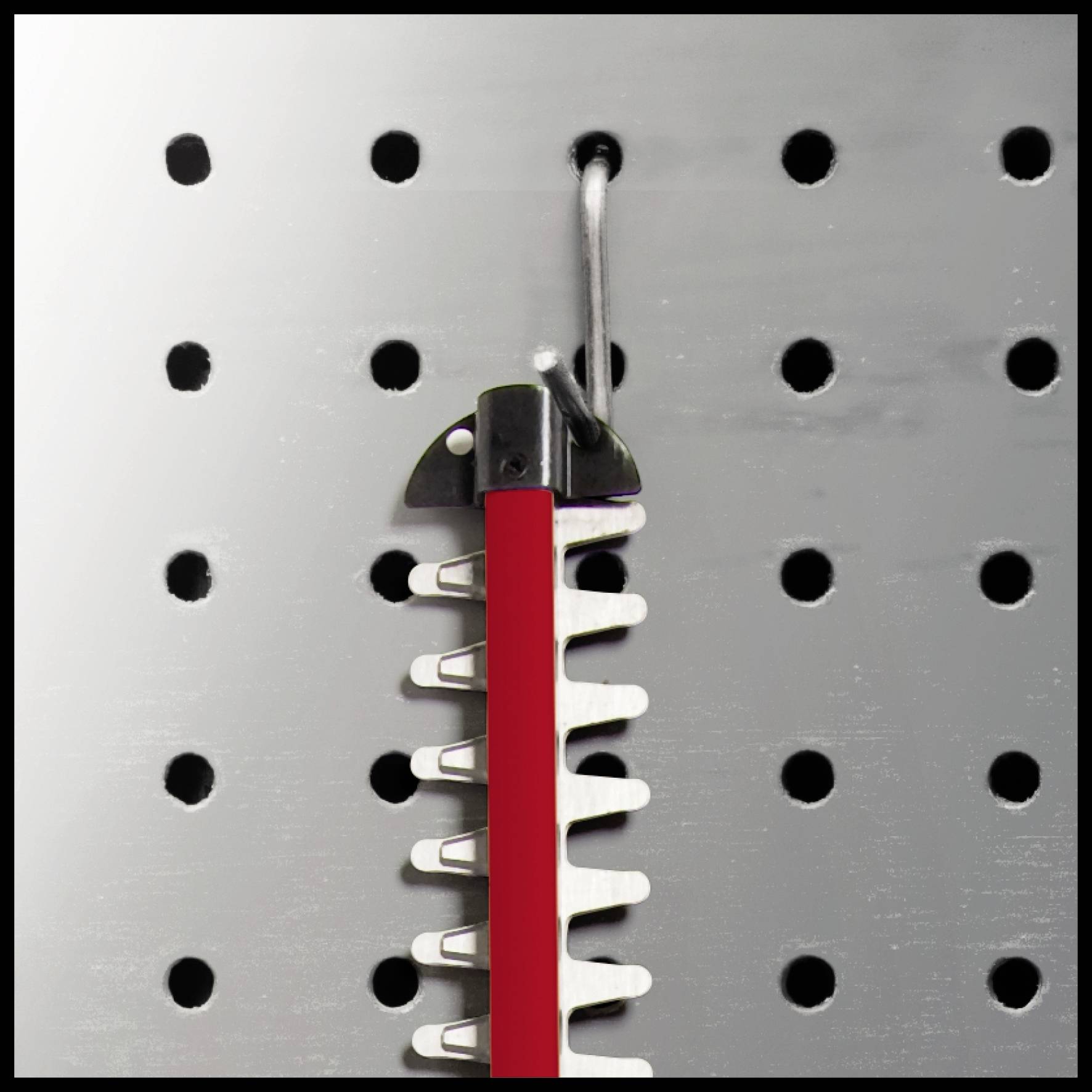 A red and black comb is hanging on a hook against a perforated metal wall.